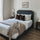Upholstered bed with dark paneled headboard styled with layered white bedding, brown accent pillows, and a textured taupe throw in a bright, modern bedroom, emphasizing a cozy setup with wood nightstands and soft natural light.