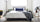 Bright bedroom with a modern black platform bed, crisp white bedding, a blue accent pillow, and surrounding plants that add a fresh, minimal feel to the space.