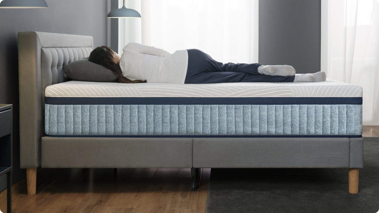 Person lying on side on hybrid mattress with textured top and blue side panels, showing full-body support in a modern bedroom