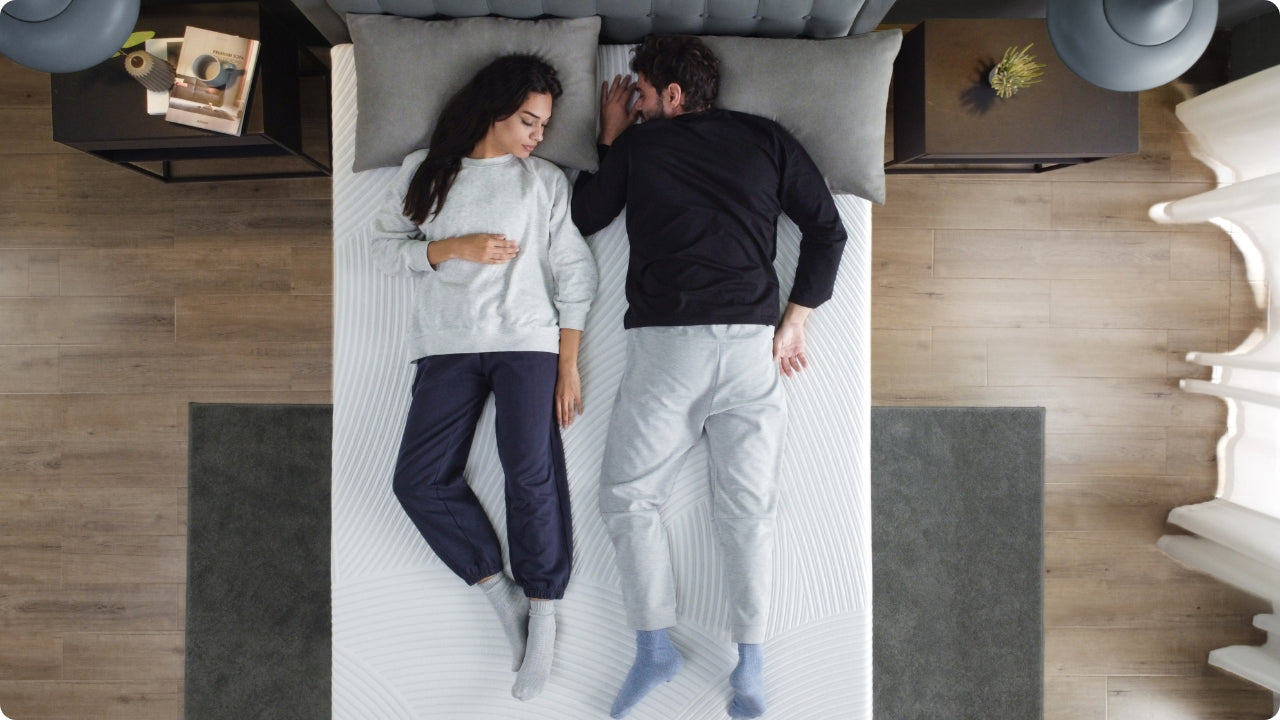 Couple resting on a textured memory foam mattress in a modern bedroom, showing comfortable support and stable surface that keeps each sleeper settled while highlighting a clean, minimalist setup with nightstands and soft lighting.