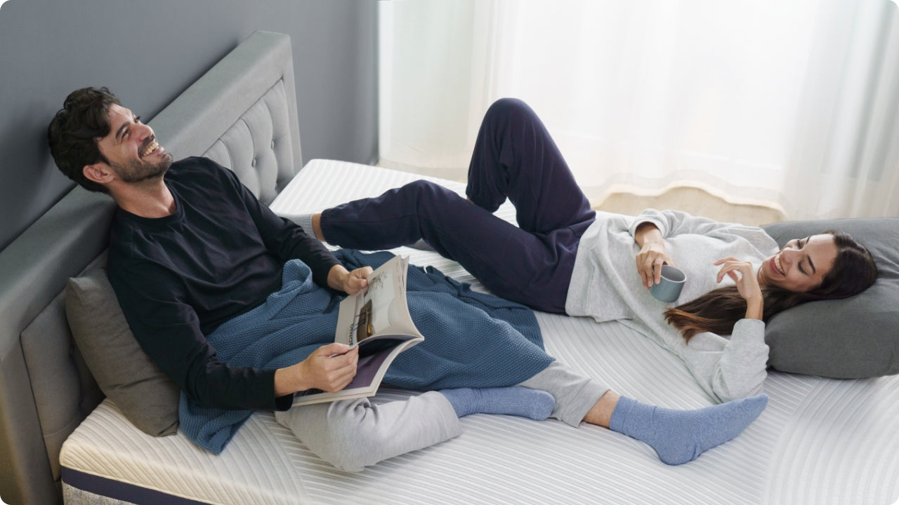 Couple relaxing on a zoned foam mattress, showing cushioned surface comfort and stable support while they read and unwind together.