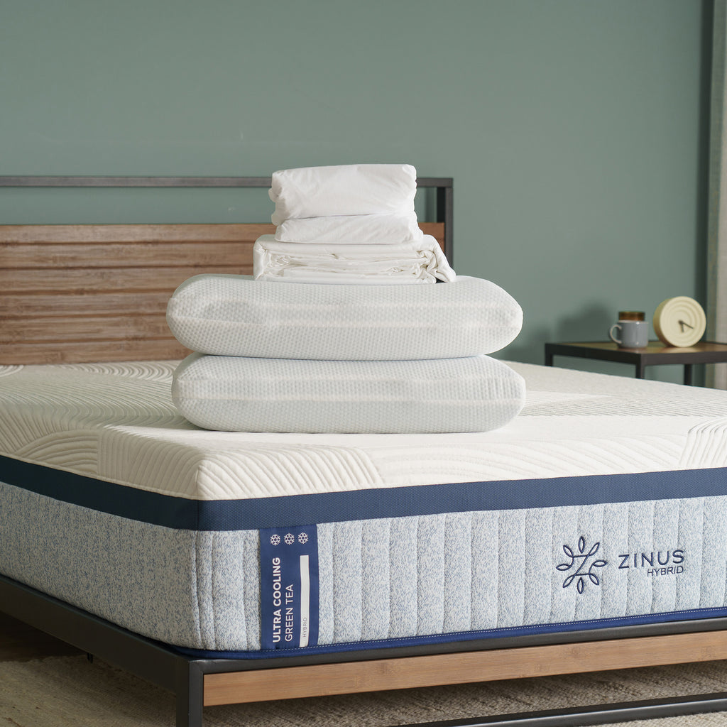 Sleep Green Bed Bundle displayed on a Zinus Hybrid Ultra Cooling Green Tea mattress, featuring white bamboo sheet set with fitted and flat sheets plus two pillowcases, waterproof mattress protector, and set of two cooling memory foam pillows stacked neatly at the foot of the bed. 