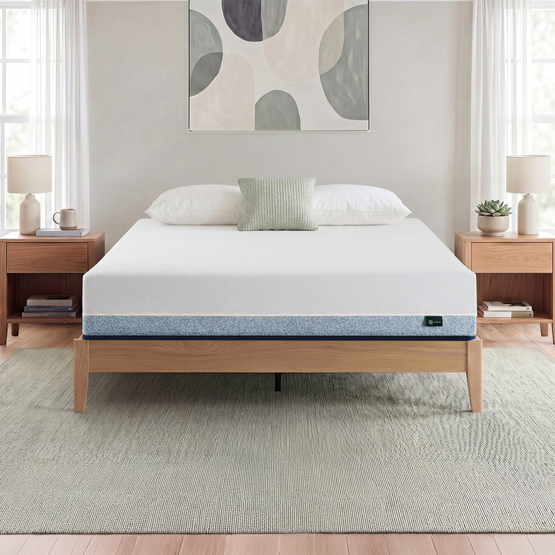 Zinus Balanced Comfort Core Hybrid Mattress fully set up on a natural wood platform bed frame in a light, airy bedroom with white and green pillows, nightstands, and lamps on either side, showing the mattress in its intended home bedroom setting.