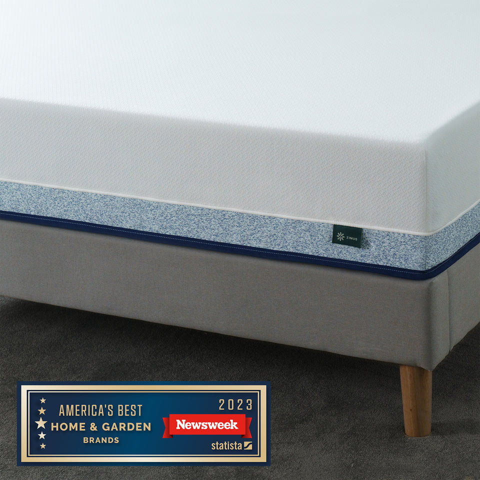 Close-up of the Zinus Original Green Tea Hybrid Mattress on a modern bed frame with light wood legs, showing textured white knit cover and supportive hybrid design. Mattress features the Zinus logo tag and is recognized by Newsweek as one of America’s Best Home & Garden Brands 2023
