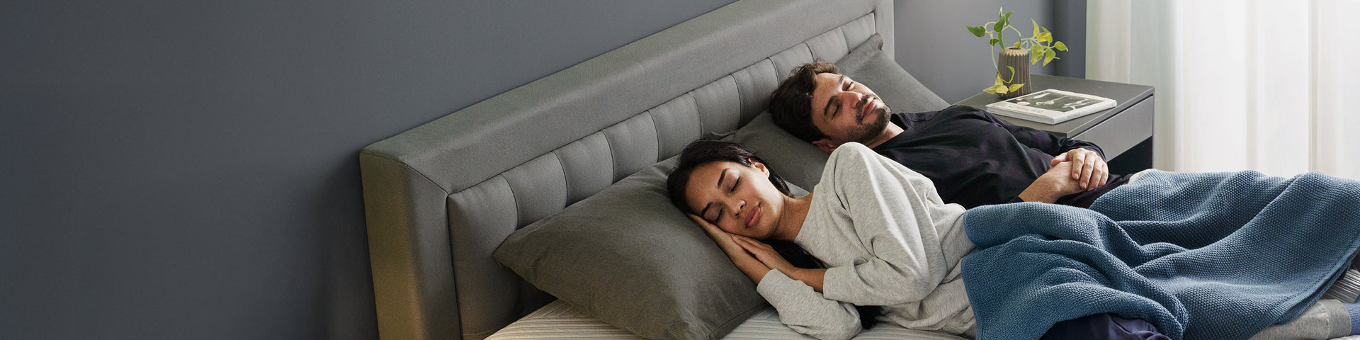 Woman in cozy white top hugs a Zinus Ultra Cooling Green Tea mattress, smiling peacefully. Bedroom setting features modern décor and gray upholstered frame. Image emphasizes mattress comfort, cooling memory foam, and deep relaxation benefits