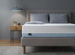 Zinus mattress with white top and blue textured side panel on upholstered platform bed frame, styled with gray pillows and blanket in a modern bedroom featuring wood nightstand, small plant, and pendant lamp, emphasizing supportive comfort and a clean minimalist design