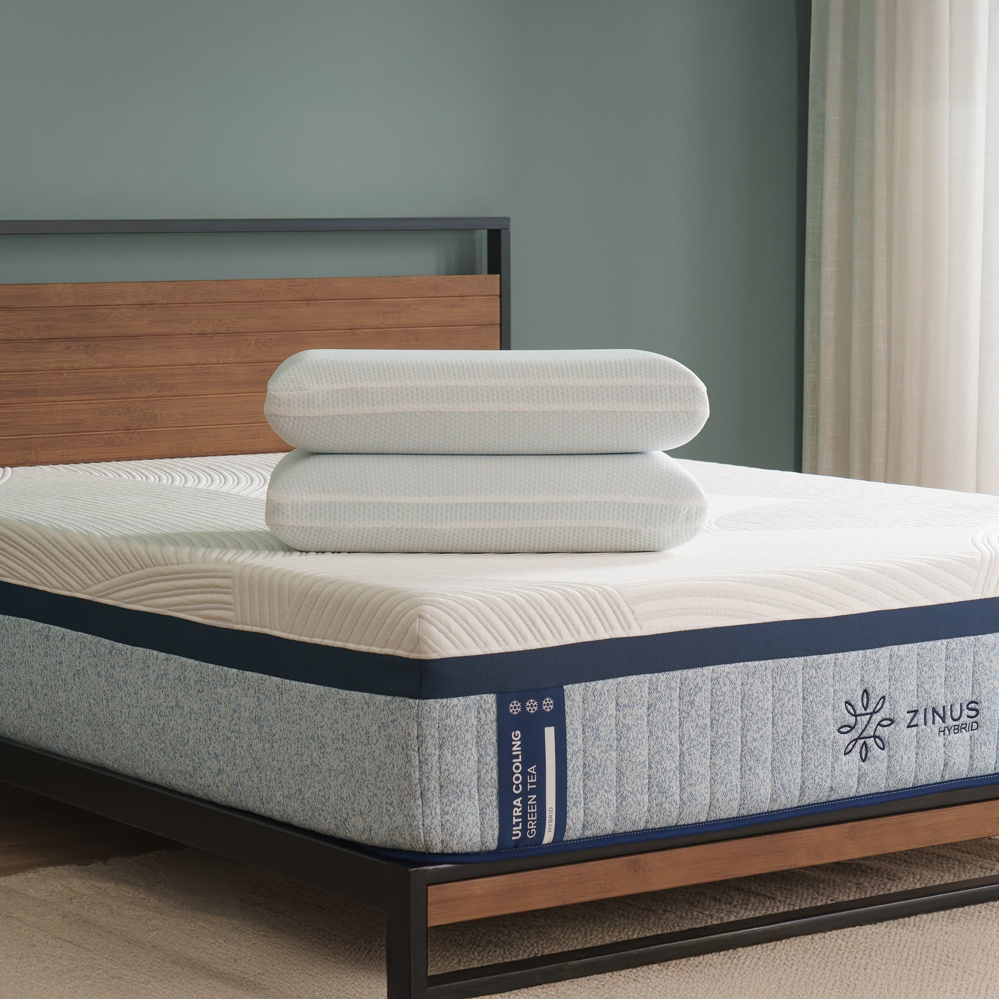 Pair of cooling memory foam pillows with breathable covers stacked on top of Zinus Ultra Cooling Green Tea Hybrid mattress, styled in bedroom with wood headboard and muted green wall.