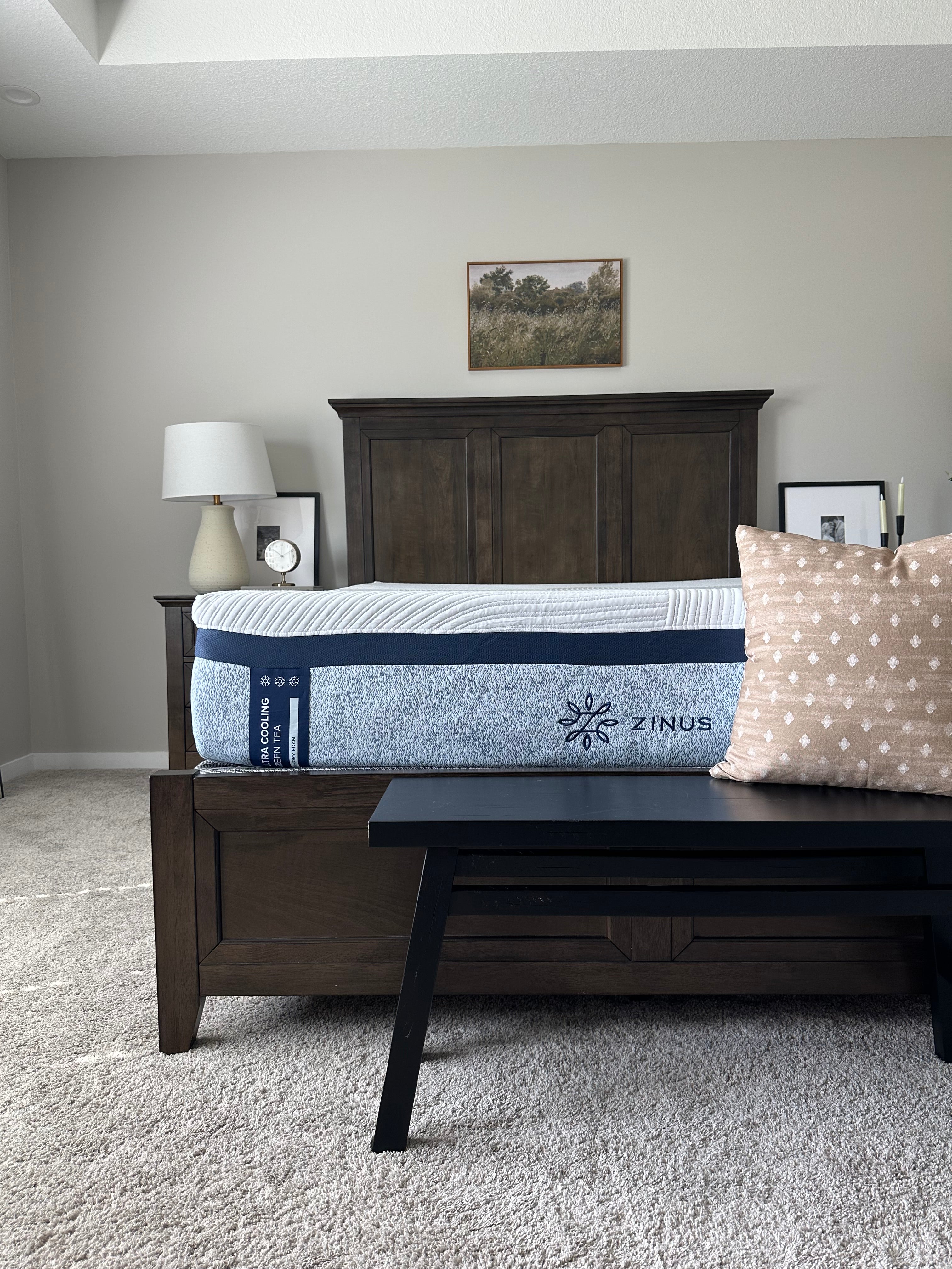 Zinus Ultra Cooling Green Tea mattress with white top and gray side panel on dark wood bed frame, styled in a neutral bedroom with beige walls, carpet, wooden bench, and framed wall art, highlighting supportive comfort and classic design