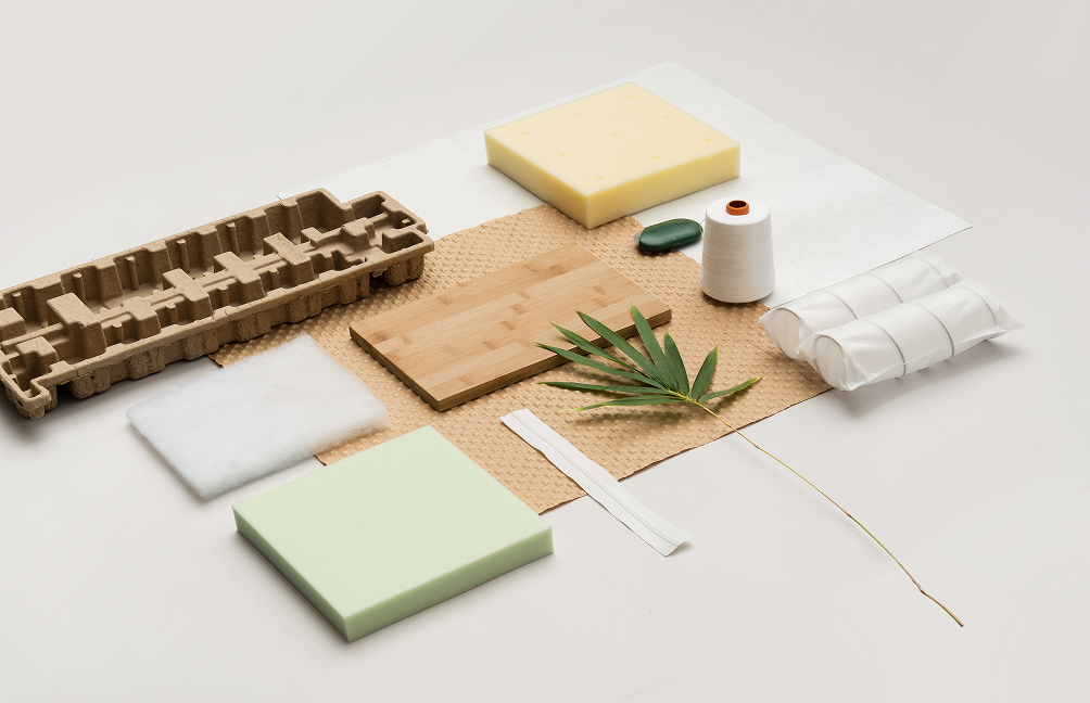 Flat lay of mattress materials including foam layers, quilted fabric, fiber fill, bamboo board, thread spool, and natural elements, illustrating thoughtfully sourced components and layered construction used in Zinus mattresses.