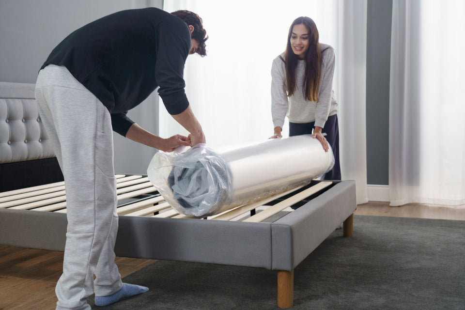 Couple unboxing Zinus Ultra Cooling Green Tea Hybrid Mattress, rolled and compressed for easy setup. The mattress expands to provide pressure relief, cooling comfort, and supportive hybrid design with memory foam and innerspring coils.