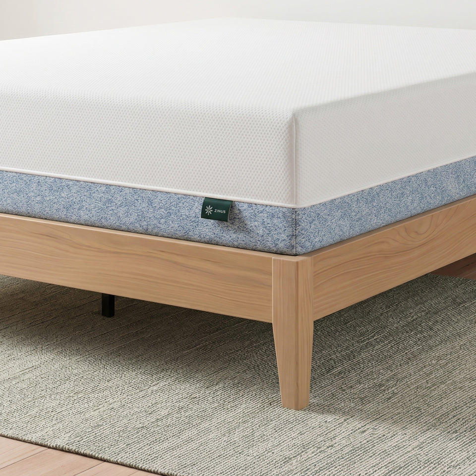 Zinus Original Green Tea Memory Foam Mattress, Queen, close-up corner detail showing white knit top cover, blue textured side panel, and Zinus logo tag, resting on light wood platform bed frame