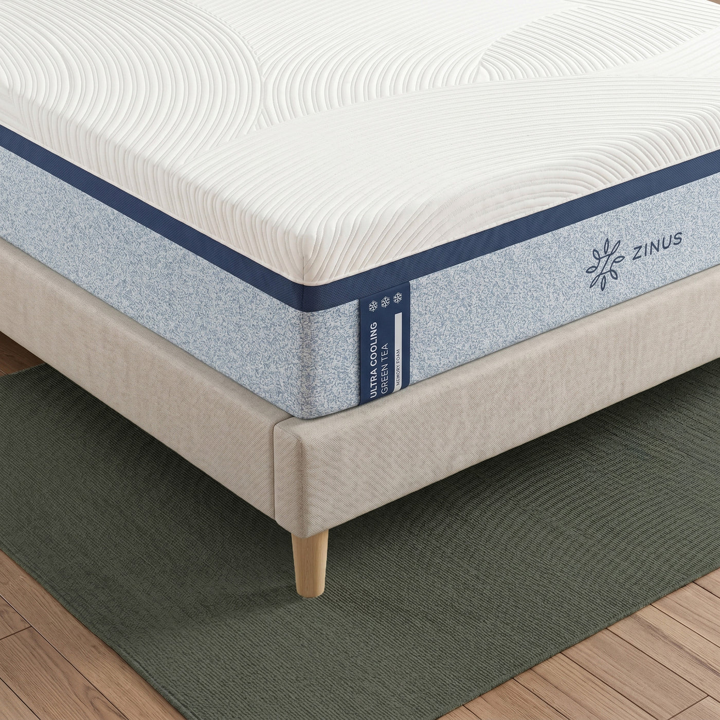 Zinus Ultra Cooling Green Tea Memory Foam Mattress, Queen, close-up corner detail on upholstered bed frame showing quilted white cover, blue textured side panel, snowflake icons, and Zinus logo.