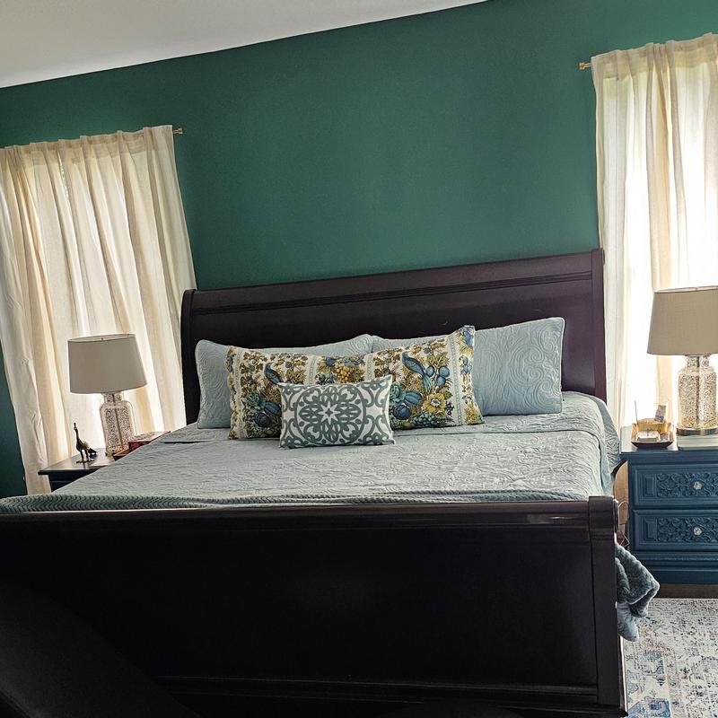 Bedroom with dark wood sleigh bed styled with light blue quilt and patterned accent pillows in front of emerald green wall, framed by cream curtains and glass lamps on blue nightstands, emphasizing classic traditional style and cozy comfort.
