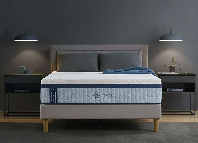 Zinus Ultra Cooling Hybrid mattress on upholstered platform bed with gray headboard, featuring supportive layers and cooling cover; styled in a dark modern bedroom with pendant lights, gray bedding, and twin nightstands