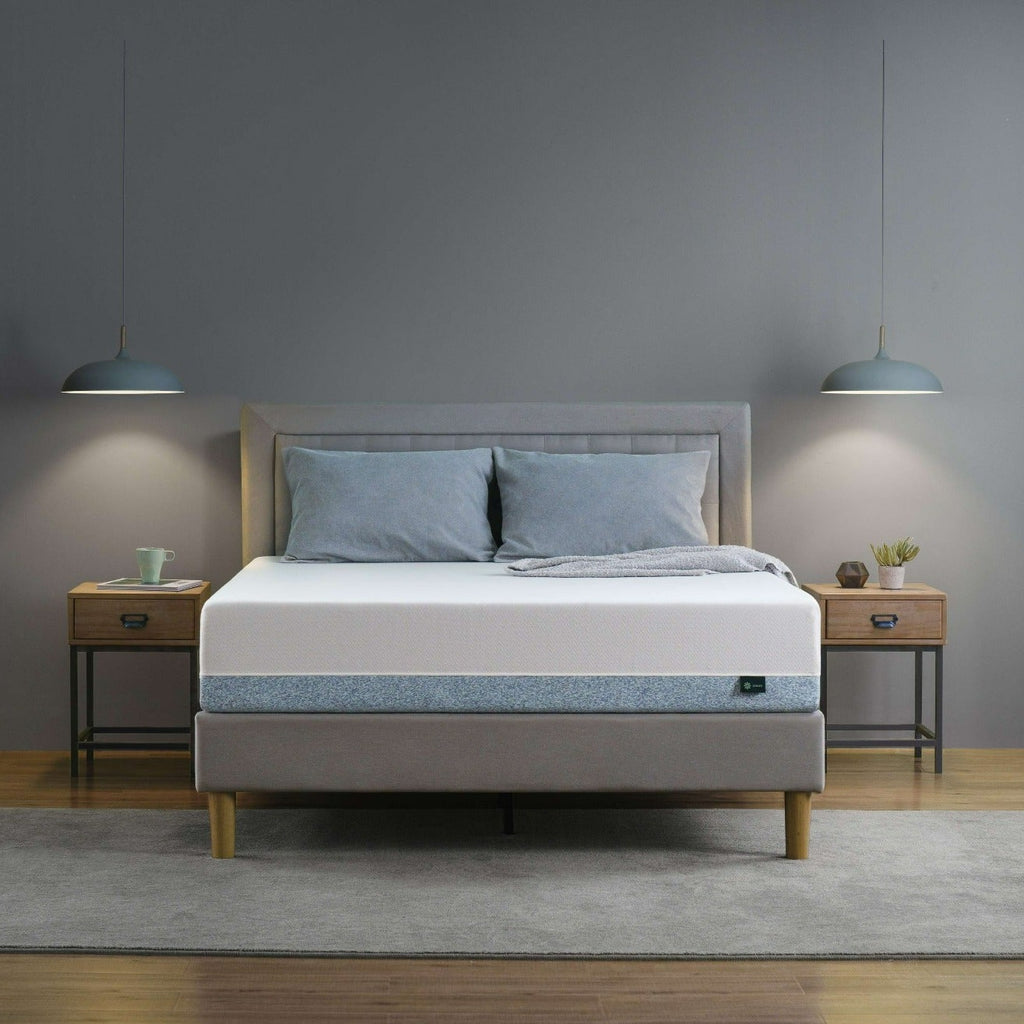 Zinus Original Green Tea Memory Foam Mattress on upholstered platform bed frame in gray bedroom, showing white knit cover with blue-gray marbled base layer, styled with blue pillows and gray throw blanket between matching wood nightstands and pendant lighting.