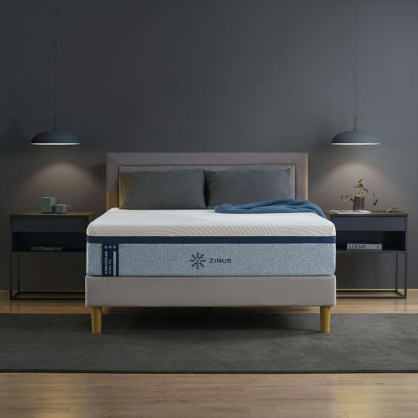 Zinus Ultra Cooling Green Tea Memory Foam Mattress styled in a modern bedroom with gray upholstered bed frame and wood legs. The mattress features blue accent side panels and a smooth cooling cover, designed to regulate temperature, ease pressure points, and support deep sleep