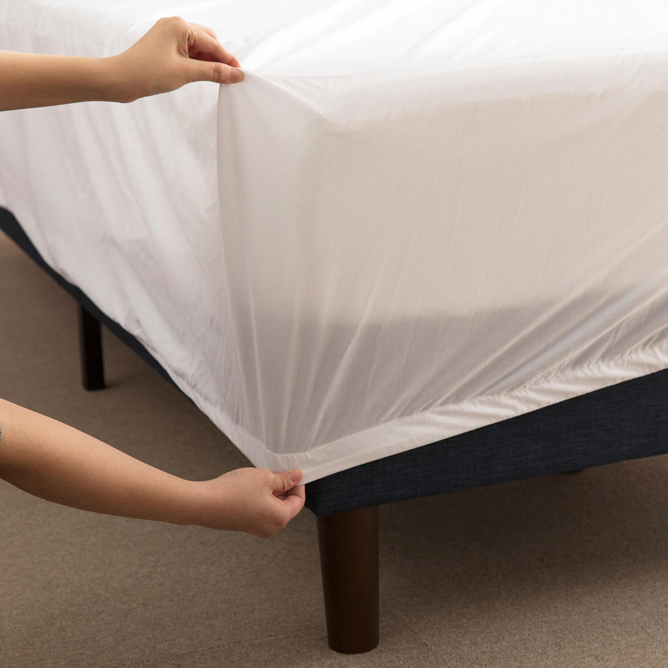 Zinus TENCEL waterproof mattress protector being stretched over a mattress corner, showing snug elastic fit. White breathable fabric protects against moisture, dust, and allergens, offering an easy-to-use shield that preserves the durability and comfort of foam or hybrid mattresses