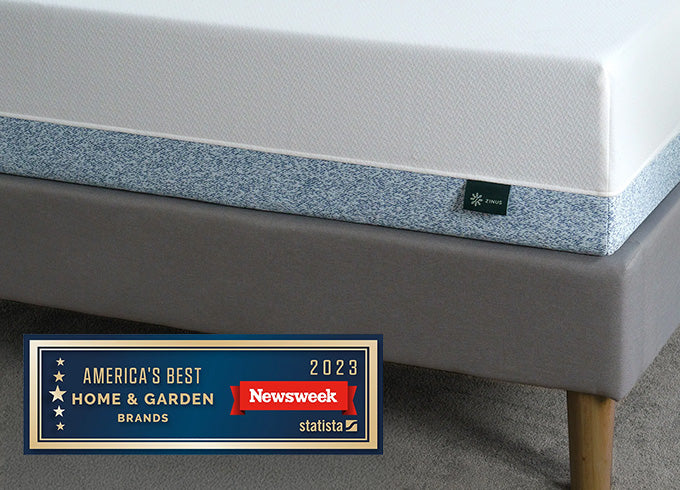 "Close-up of Zinus Cooling mattress with white top and blue speckled side panel, on upholstered bed, featuring Newsweek 2023 America's Best Home & Garden Brands award badge