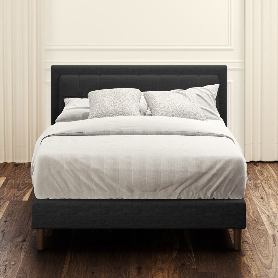 Front view of Zinus Dachelle Upholstered Platform Bed Frame in dark gray with square tufted headboard. Styled with neutral bedding in a modern bedroom, this sturdy platform bed provides lasting mattress support and elegant design.