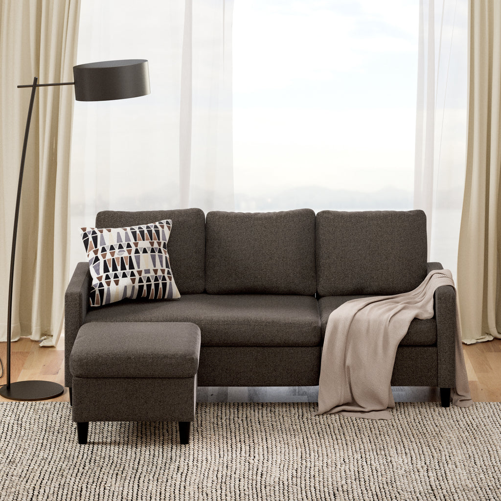 Styled living room with Zinus Hudson Convertible Sectional Sofa featuring reversible chaise and versatile ottoman in gray fabric. Sofa is accessorized with a geometric throw pillow and beige blanket, highlighting its compact, modern design that fits perfectly in bright, airy spaces 