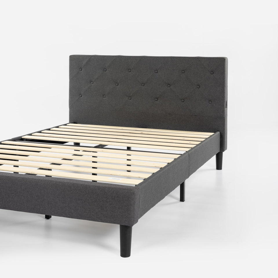 Angled side view of Zinus Upholstered Platform Bed Frame with tufted gray headboard and wood slat foundation. Sturdy structure with upholstered frame blends modern style and functionality, designed for strong mattress support and a sophisticated bedroom centerpiece.