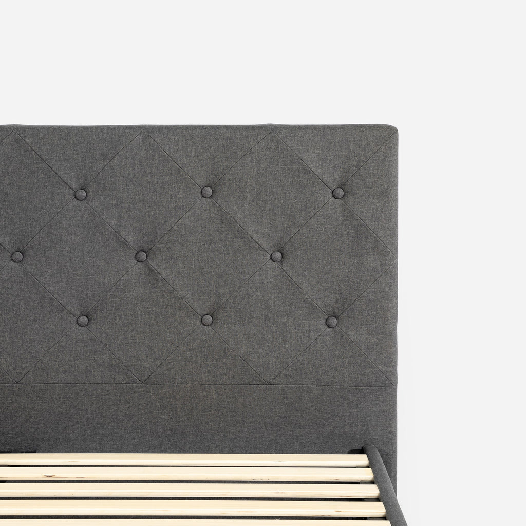Close-up of Zinus Upholstered Platform Bed Frame tufted headboard in gray linen-like fabric. Diamond-stitched pattern with fabric-covered buttons highlights refined style and durability. Padded design adds comfort while enhancing the bed’s modern and timeless look 